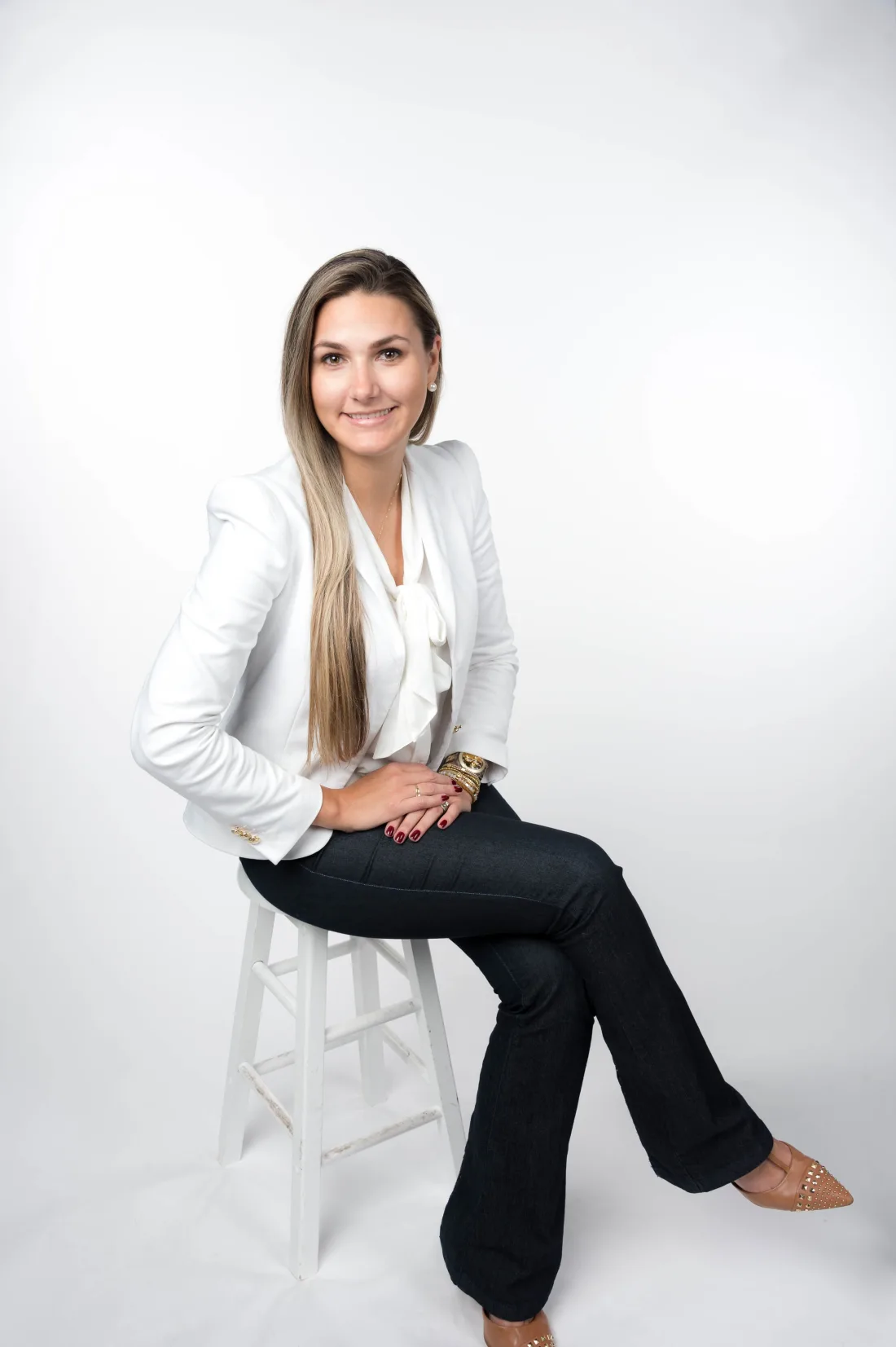 Mariani Sirianni sentada em um banco, sorrindo, com blazer branco